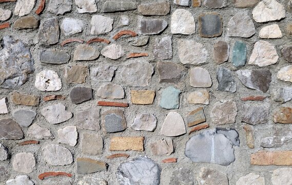 Concrete wall with stones of various sizes, shapes, colors, and fragments of bricks and roof tiles randomly embedded in the structure. Background and texture