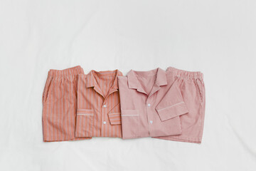Top view two striped cotton pajama set shirt and shorts in pastel pink red color on white bed...