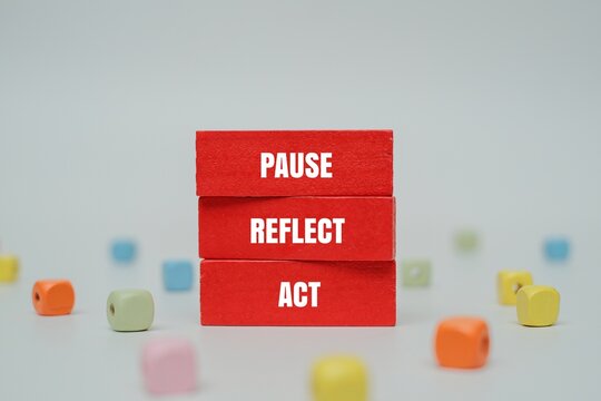 A coloured blocks with text PAUSE, REFLECT, ACT surrounded by colorful beads. The framework of intentional living or mindful leadership concept