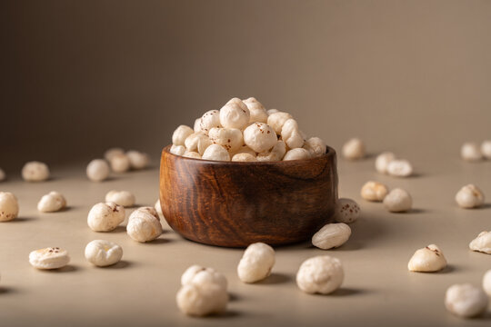 Phool Makhana, Fox Nut, Lotus Pops Seeds, Gorgon nut, Euryale Ferox on a wooden bowl with beige background.