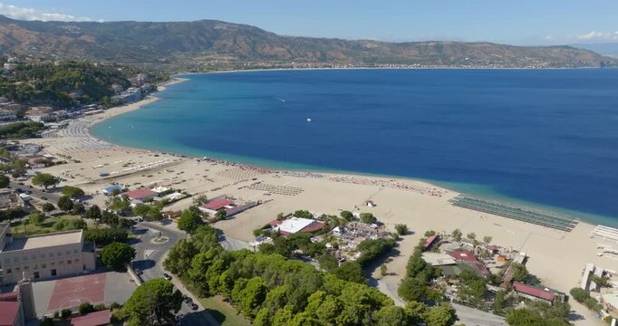 Aerial panorama of a wide sandy beach with organized sunbeds and umbrellas and a calm blue sea. It is the waterfront of Soverato, located in the province of Catanzaro, in Calabria, Italy.