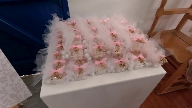 Small gift boxes are neatly placed on a table, wrapped with tulle and ribbons, ready for guests. The setting has wooden furniture and a blue door.