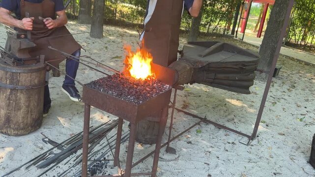 Blacksmith uses bellows to heat metal in forge, traditional craft