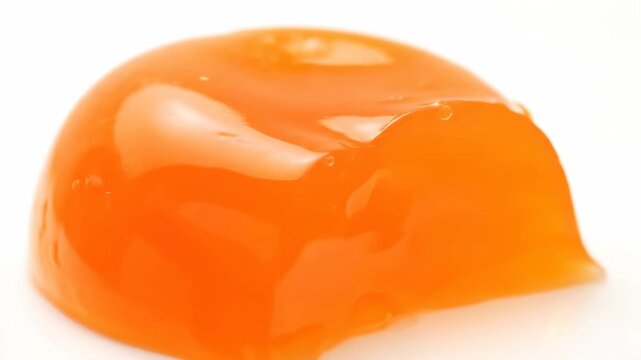 Appetizing bright orange gelatin dessert piece, shiny and translucent, cut into a dome shape and isolated on a white studio background with copy space.