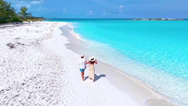 Aerial view of a happy vacation couple walking on a tropical beach with turquoise shining ocean, Exuma islands, Bahamas, Caribbean