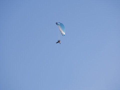 Person flying in a powered parachute over a clear blue sky on a sunny day.