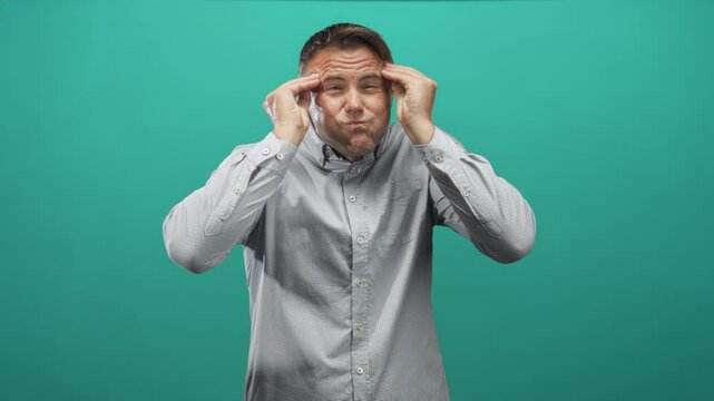Man presses temples, puckers cheeks and gestures with raised hands in studio; frustration concentration.