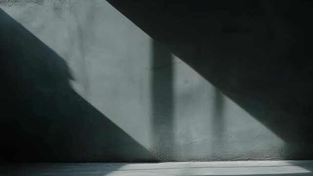 Empty minimalist room featuring natural light creating striking diagonal and vertical shadows across a textured grey wall and rough floor, highlighting stark contrast and depth