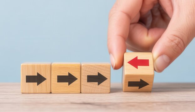 Hand changing direction of wooden block arrow from right to left, concept of change, decision making or going against the flow