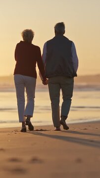 Elderly couple walking on beach at sunset