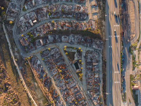 Aerial view of destruction and desolation where homes used to stand starkly contrasts with the adjacent highway's bustle, Pacific Palisades Bowl, California, United States.