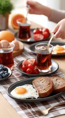 A young boy cooks fried eggs for breakfast and serves black tea while various foods are arranged on the table