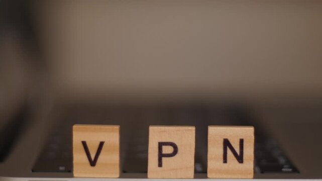 Child hand arranging wooden blocks spelling VPN with laptop blurred in background, shallow depth of field