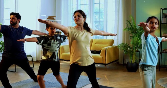 Indian family doing virabhadrasana yoga at home practicing warrior pose together indoors for healthy body and calm mind during morning routine inside a modern lavish living space
