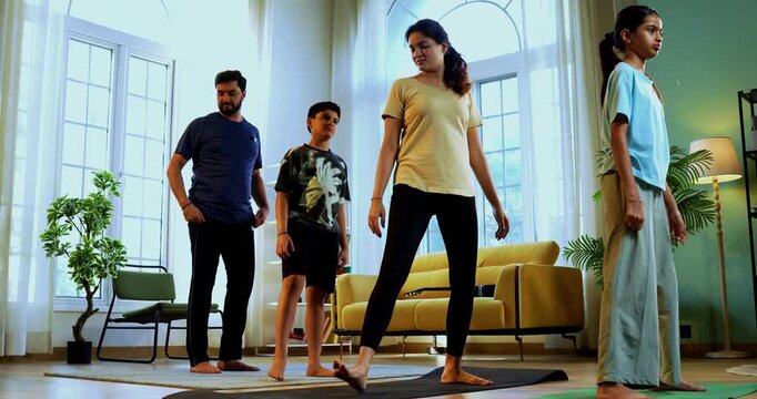 Indian family doing virabhadrasana yoga at home practicing warrior pose together indoors for healthy body and calm mind during morning routine inside a modern lavish living space