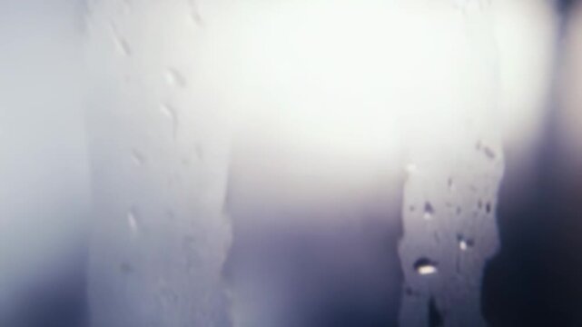 Water drops accumulating on a glass surface creating a textured background with natural light shining through, showing condensation and liquid patterns