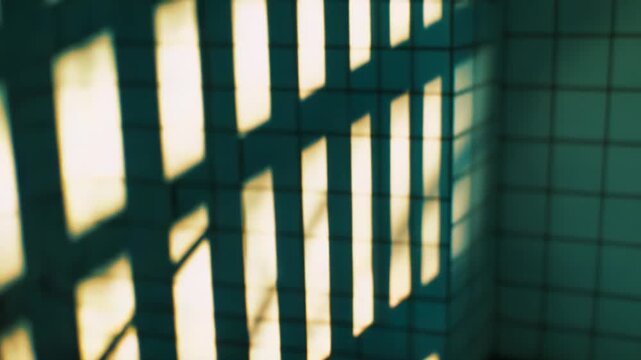 Golden light creating a stark pattern of shadows from vertical and horizontal bars on a tiled wall and floor, evoking feelings of isolation, hope, and confinement within a minimalistic space