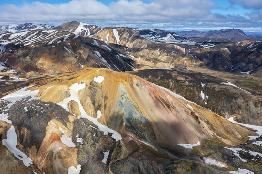 Aerial view of the surreal, ochre and crimson-streaked rhyolite mountains, dusted with snow, create a painterly tapestry under a vast sky, Rangarthing ytra, Iceland.