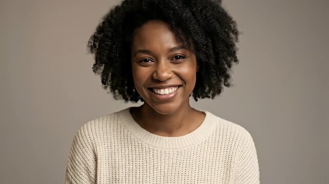 A radiant close-up portrait of a young adult with beautiful dark, curly hair and a warm complexion, looking directly at the camera with a genuine, wide smile. The cheerful expression conveys joy, conf
