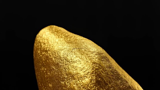 Close-up of a shimmering gold nugget against a black background. Represents wealth, luxury, and the allure of precious metals