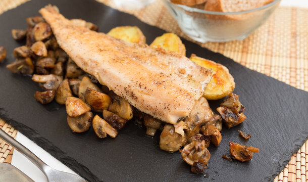 fried trout fillet on pillow of fried champignon mushrooms on dark warm stone plate