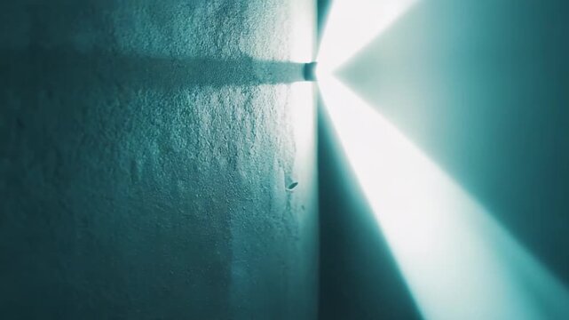 Light emitting a bright glow from a small fixture, illuminating two perpendicular textured walls within a dark interior space, creating an abstract background