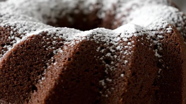 Close-up of rich dark chocolate bundt cake dusted with white powdered sugar, showcasing the moist cocoa texture and dramatic moody aesthetic of the gourmet bakery dessert.