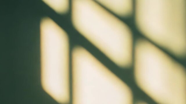 Sunlight streams through a window, casting an artistic pattern of square and rectangle shadows on a muted green wall, forming an abstract and minimalist background