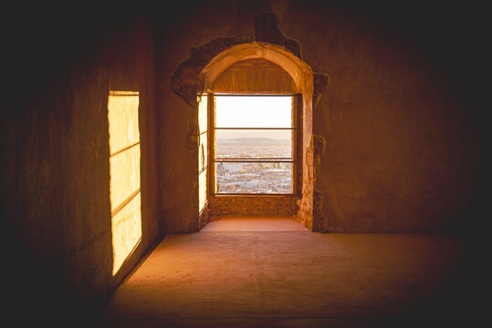 View of light streaming through arched windows, illuminating an empty room with a distant cityscape under a soft sky, Granada, Andalusia, Spain.