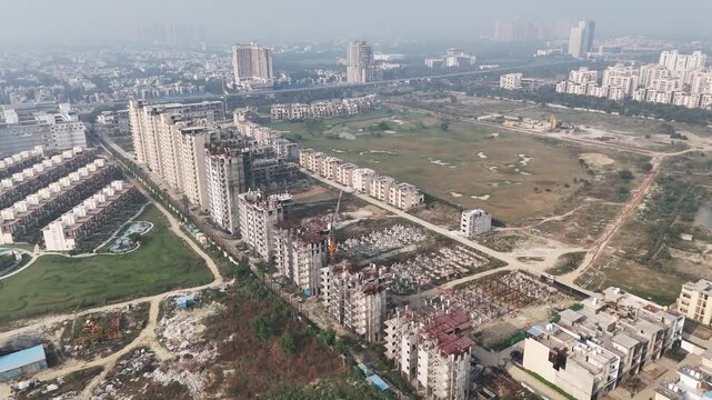 Wide aerial panorama of a growing Noida neighborhood, featuring construction activity, modern housing rows, and emerging infrastructure amid surrounding greenery.