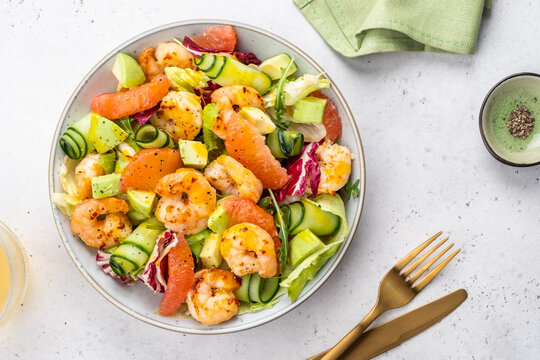 Fresh shrimp salad with colorful vegetables and dressing served in a bowl on a kitchen table