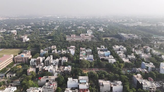 Aerial view of Greater Noida showcasing low-rise residential neighborhoods, tree-lined streets, and an open green playground under light haze, reflecting calm suburban city life.