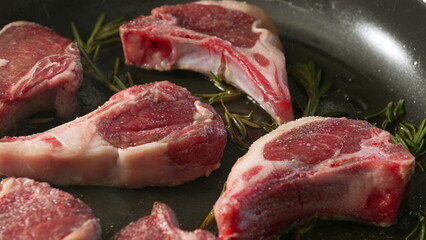 Raw lamb chops seasoned and arranged on pan with sprigs of rosemary before cooking, showing detailed texture and marbling of fresh uncooked meat