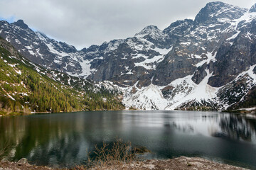 Morskie Oko lake surrounded by snow-capped Tatra Mountains in Poland, featuring lush green forests and a tranquil water surface reflecting the dramatic landscape © mikeosphoto