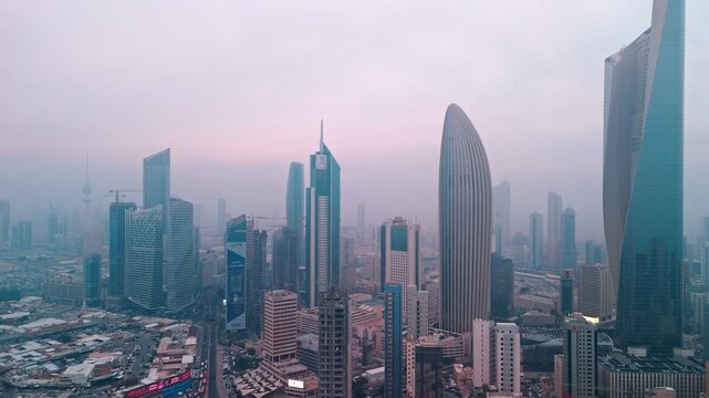Drone view of kuwait city downtown skyline in morning haze, iconic modern towers and business district under a soft pink sunrise sky for urban, finance, travel visuals.