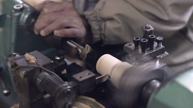 Spinning wood lathe drilling and cutting a wooden piece, woodworker's hands close up