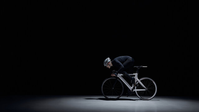 Cyclist riding road bike under dramatic studio lighting. Concept of elite cycling, intense training, speed performance, professional sport, focus and discipline, dark minimal background.
