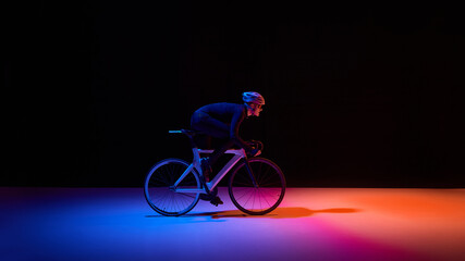Fototapeta premium Professional cyclist riding road bike under neon lighting with copy space. Concept of sports branding, performance marketing, insurance campaigns, fintech visuals, digital innovation, and control.