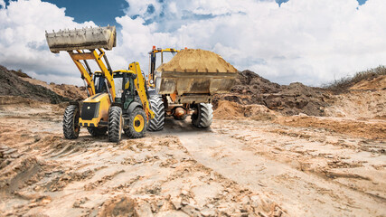 Obraz premium Construction equipment - two front-end loaders - moves soil across a construction site; earth embankments are visible in the background, indicating an active construction site