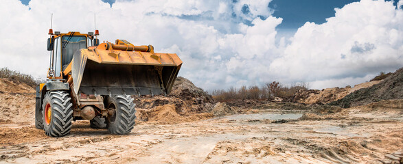Construction site shows dry, cracked earth with dirt mounds and a loader ready to work under a partly cloudy sky © Anoo