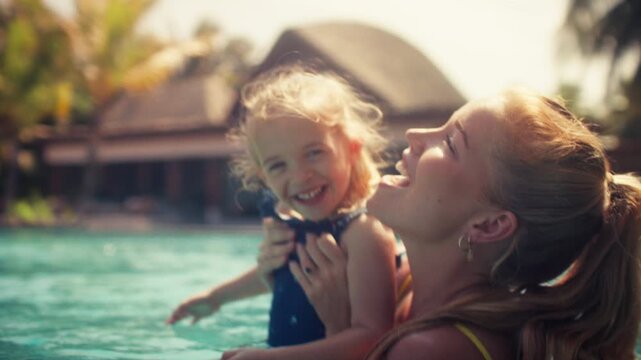 Joyful mother and daughter playing happily in a luxurious resort swimming pool during vacation