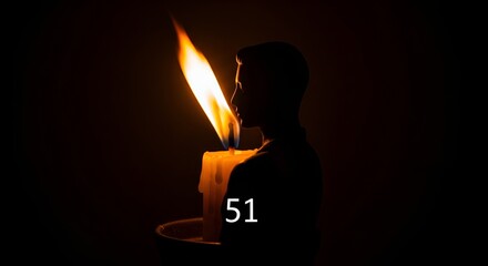 Silhouette of a person holding a lit candle in the dark, creating a warm glow.