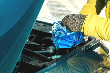 Pouring winter windshield washer fluid into car engine compartment