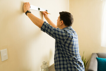 Man measuring and marking a wall with a spirit level and pencil, performing do it yourself work at...