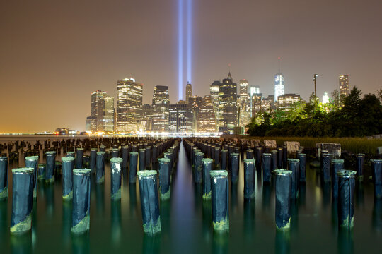 View of the Tribute in Light pierces the night sky above the glittering cityscape, reflecting in the serene water, a poignant reminder, New York, New York, United States.