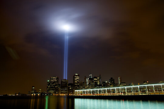 View of two bright beams of light rising high into the night sky from the city's dark skyline, reflecting on the calm waters, New York, New York, United States.