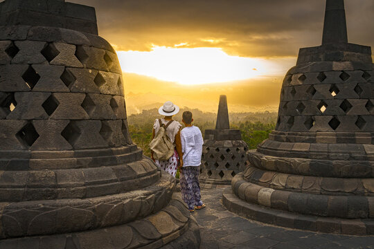 View of a woman and a child silhouetted against the fiery sunset between ancient stupas, Borobudur Temple, Magelang, Central Java, Indonesia.