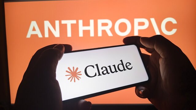 A person holds a smartphone with the Claude logo in front of an orange screen displaying the word Anthropic.