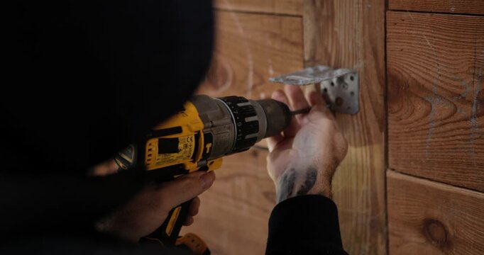 Craftsman at Work: Focused craftsman uses a power drill to meticulously attach a metal hinge to a wooden structure, showcasing precision and craftsmanship in their work.