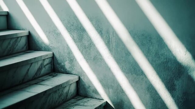 Sunlight beams through a window, creating strong parallel shadows on a teal colored textured wall and gray marble stairs, evoking feelings of progression and anticipation
